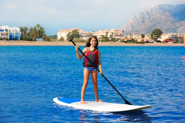 Kid paddle surf surfer girl with row in the beach