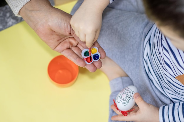 kid paints a easter egg with watercolor helped by the grandma easter holiday home activities