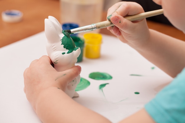 Il bambino dipinge la figura di un coniglio con vernice verde