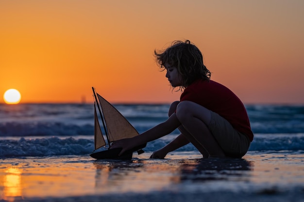 写真 子供は晴れた日にビーチで遊ぶ小さな船員が海水で帆船で遊ぶ子供の夢