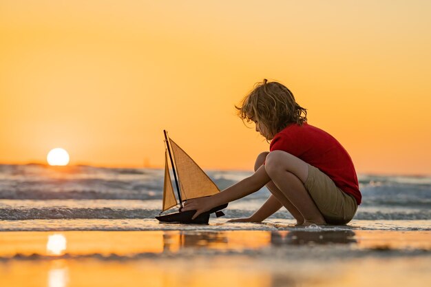Foto bambino che gioca sulla spiaggia bambino che gioca sul mare con una barca giocattolo bambino che ha un momento felice
