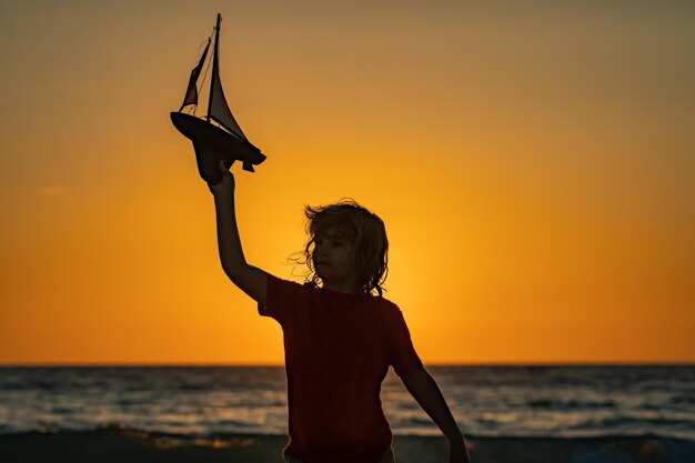 ビーチで遊ぶ子供 遊びのボートで遊ぶ子ども 夕暮れの海で遊びの子供