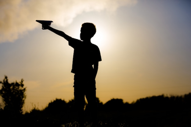 Foto bambino che gioca con l'aeroplano di carta al tramonto