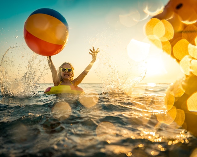 Photo kid playing with rubber duck and ball in the sea.