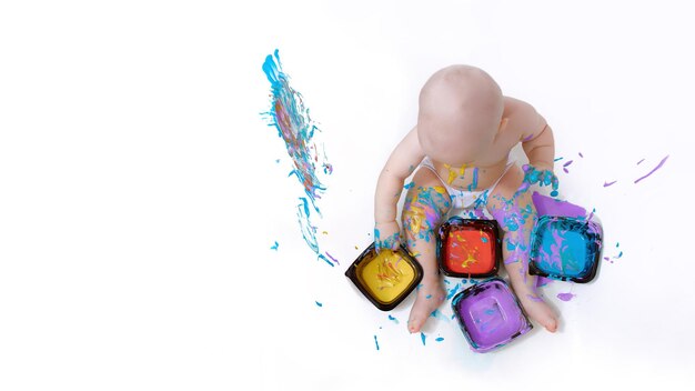 The kid plays with paint getting dirty with it on a white background with a place to copy the text