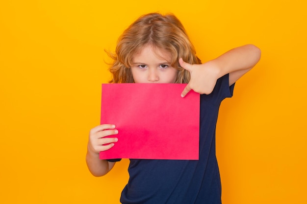 Kid pointing on empty sheet of paper isolated on yellow background portrait of a kid holding a blank