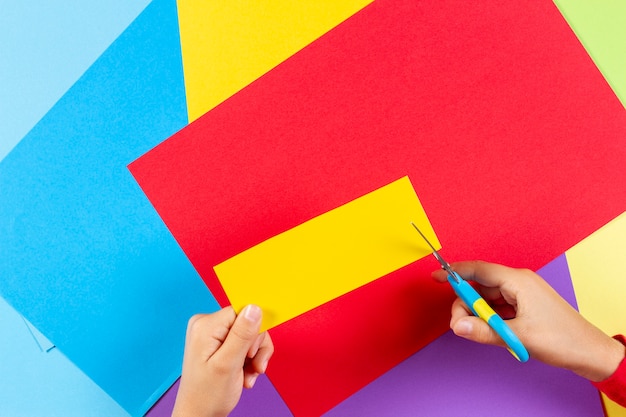 Foto mani del bambino che tagliano carta colorata con le forbici