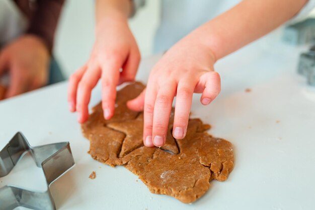 ジンジャーブレッドを作る子供の手、ジンジャーブレッド生地のクッキーを切る。お祝い料理、調理プロセス、家族の料理、クリスマスと新年の伝統のコンセプト