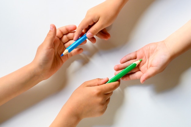 Kid's hands share each other colored pencils on a white