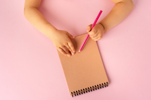 Kid's hands writing in open notebook, top view, copy space