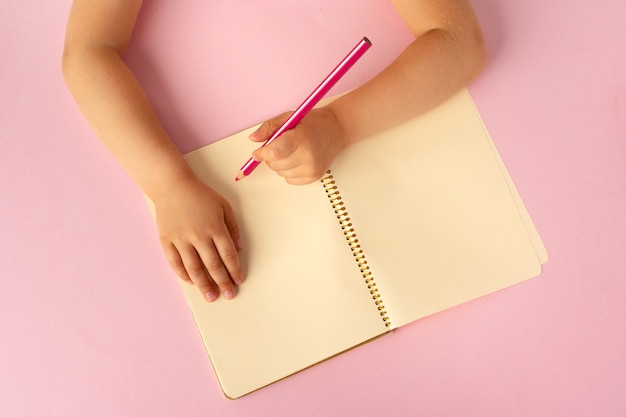 Kid's hands writing in open notebook, top view