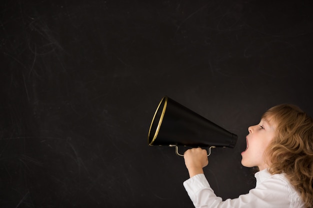 Kid shouting through vintage megaphone against blackboard