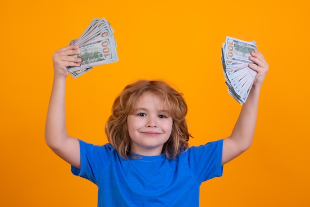 Kid showing money dollar bills standing dreamy of rich against isolated yellow studio background