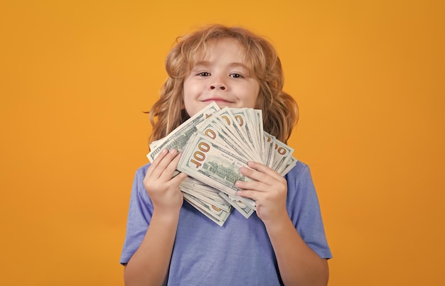 Photo kid showing money dollar bills standing dreamy of rich against isolated yellow studio background