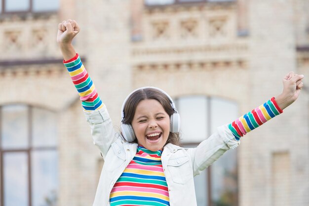 子供は校庭で歌います。ポジティブでカラフル。子供は音楽の休憩があります。ヘッドフォンの女の子。かわいい女の子はワイヤレスヘッドセットを着用します。学校に戻る。新しいテクノロジーによる現代教育。