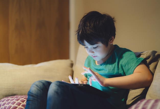 kid siting on sofa watching cartoon on tablet