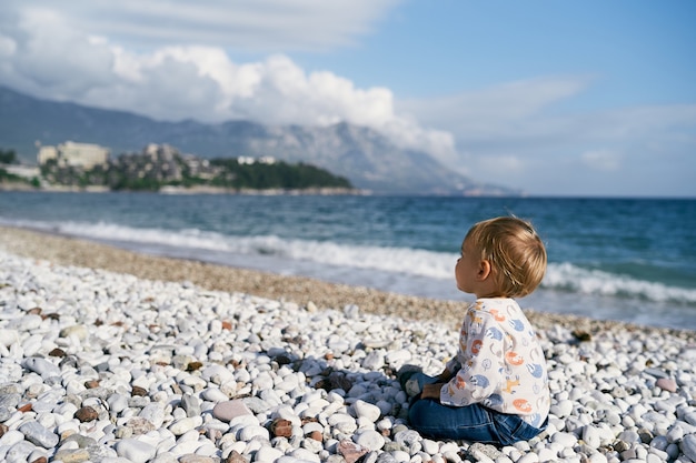 写真 子供は海側の景色の小石のビーチに座っています