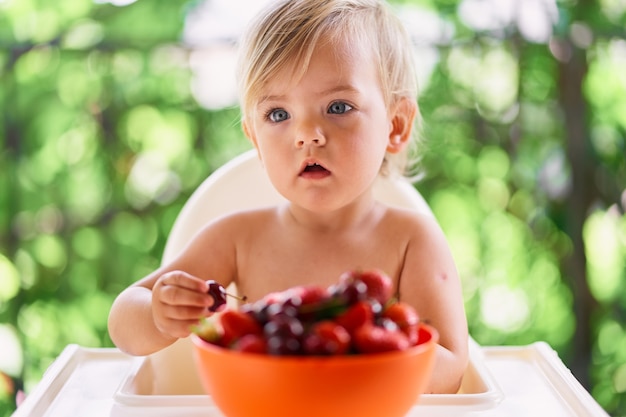 子供は皿の上のさくらんぼの前のバルコニーのテーブルに座っています