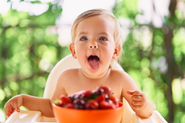 子供は果物のボウルの前のテーブルに座っています