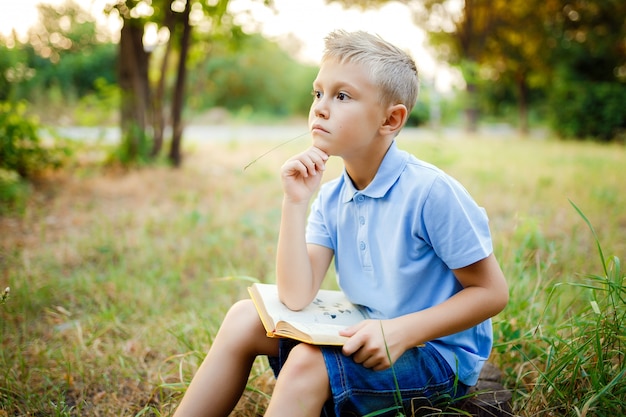 Kid sitting in the forest with book on the knees and looking away.