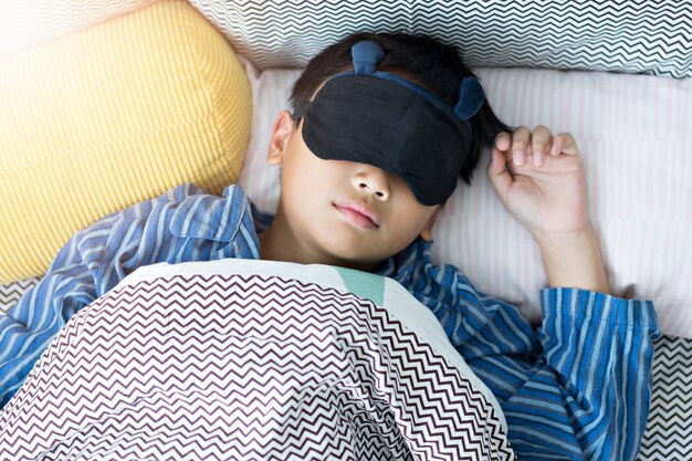 Kid sleeping in bed under the blanket at home.