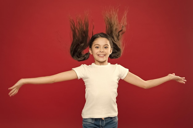 Kid smiling cute face live carefree happy life Enjoy every moment Young and free Happy child girl with long hair on red background Happiness and joy Positive emotions Child care and upbringing