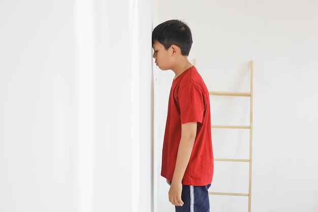 両親に罰せられて壁の前に立っている子供は悲しみを感じる