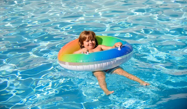 Kid in swimming pool relax swim on inflatable ring and has fun in water on summer vacation