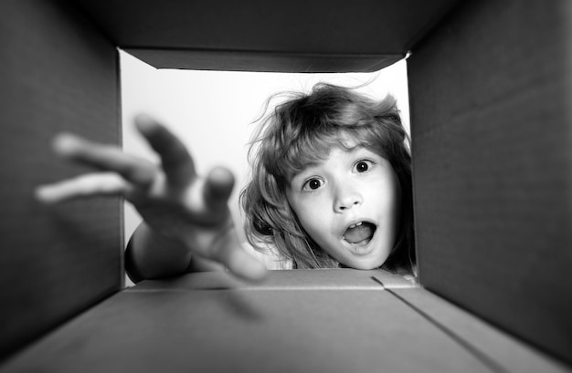 Kid unpacking and opening carton box and looking inside with surprise face child boy looking