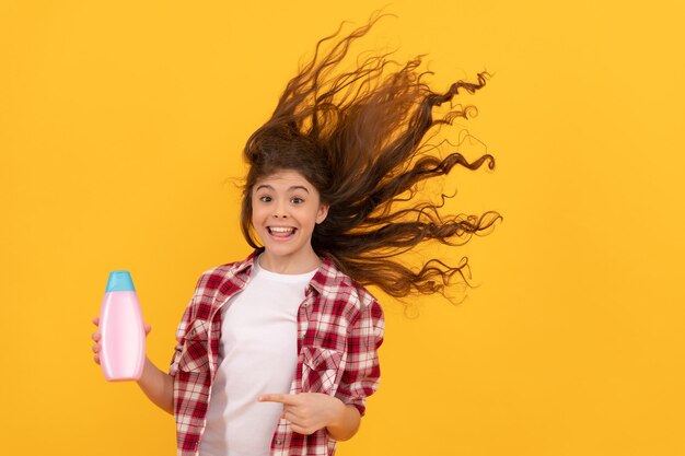 I bambini usano il gel doccia. ragazza teenager felice con la bottiglia di shampoo. shampoo per capelli in salone. bambino con balsamo. lunghi capelli ricci. abitudini quotidiane e cura della persona. presentazione del prodotto cosmetico. bellezza.