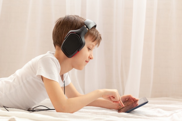 집에서 카펫에서 음악을 듣고 디지털 태블릿 및 노트북을 사용하는 아이. 개념 온라인 교육