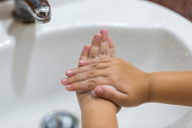 Kid wash hands with antibacterial soap foam on washbasin to prevent covid-19 new normal