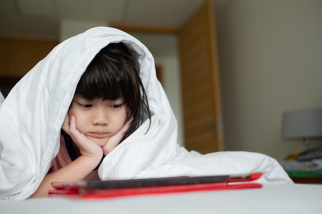 kid watching tablet on the bed at night time