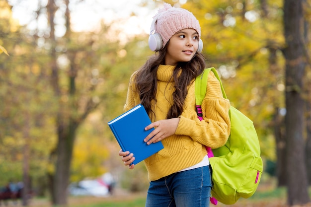 Kid with book and backpack listen music in earphones, school.