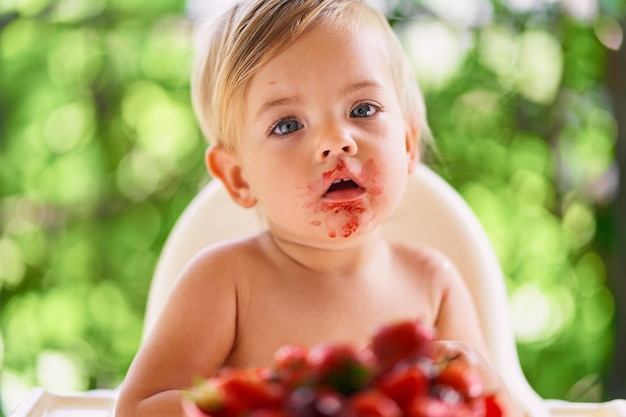 汚れた顔の子供は果物のプレートの前のバルコニーに座っています