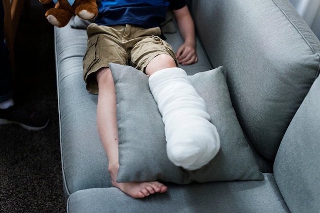 Photo kid with injured leg is sitting on the couch