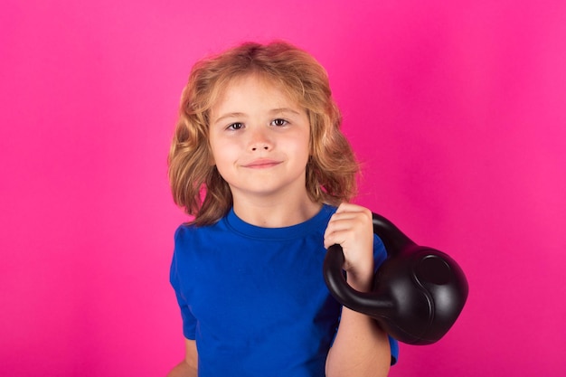 赤ピンクの背景にスタジオでケトルベルを持つ子供 かわいい子男の子 ダンベルで腕の筋肉をポンピング
