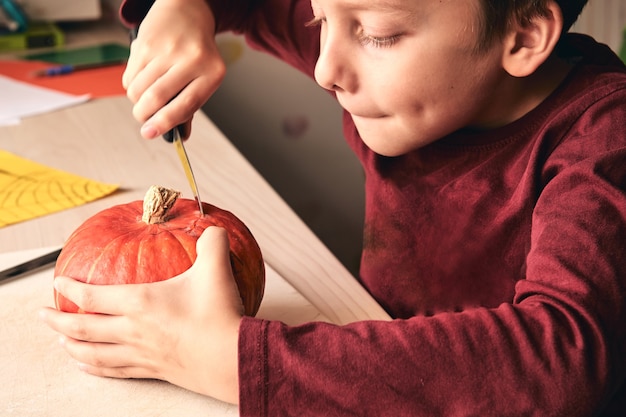 kid with knife carving pumpkin or jack-o-lantern. Mom spending time with son together.