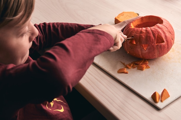 kid with knife carving pumpkin or jack-o-lantern. Mom spending time with son together.