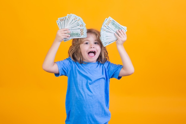 Kid with lots of money dollar banknotes isolated over yellow studio background