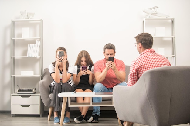 Kid with phone addicted daddy and mom sitting at psychologist\
solving problem internet