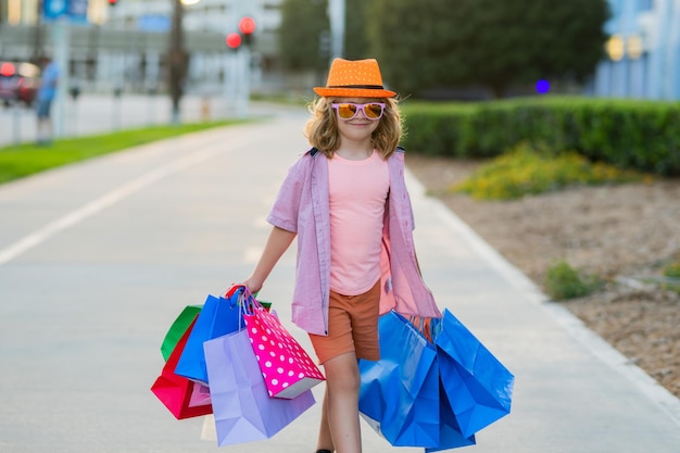 Kid with shopping bags child in trendy hat and shirt shopping near shopping center happy boy holding