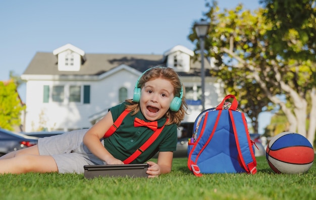Ребенок с планшетным устройством сидит на открытом воздухе в саду в шортах и рубашке Маленькая детская школа на открытом воздухе