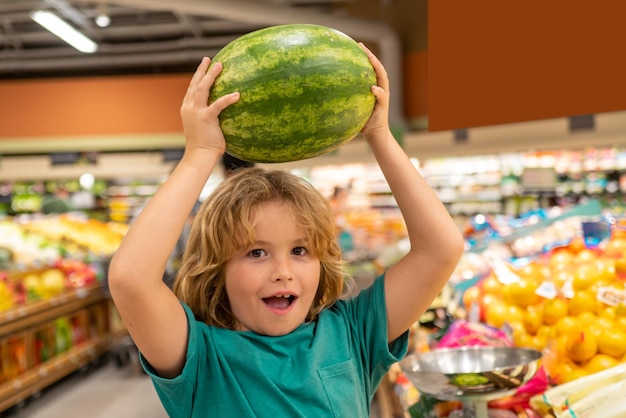 Kid with watermelon child choosing fruits and vegetables during shopping at vegetable supermarket