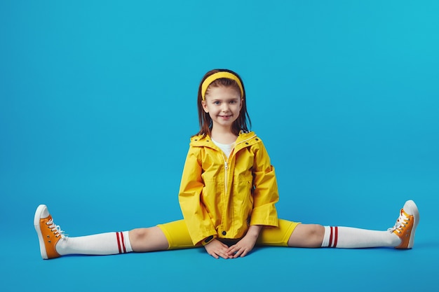 Ребенок в желтой одежде делает упражнения на растяжку шпагатом позы под прямым углом