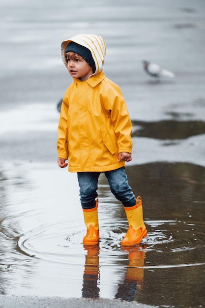 비가 온 후 야외에서 노는 노란색 방수 망토와 부츠를 입은 아이