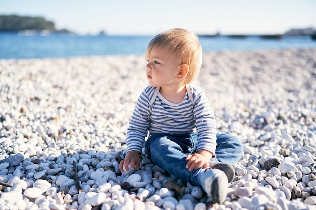 Kid zit op een kiezelstrand aan zee en kijkt in de verte