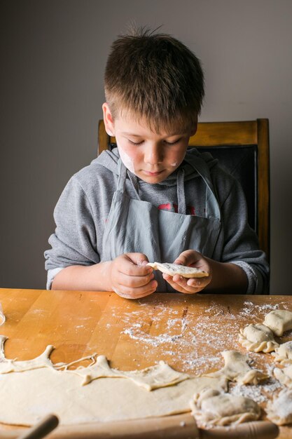 Kidboy making dumplings pierogi varenyky served with cottage cheese lay in sieve National Ukraine cuisine natural organic homemade bakery product