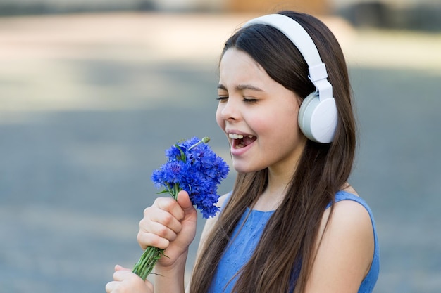 Kiddie song. Happy kid sing song outdoors. Using flowers as microphone. Little child enjoy singing in headphones. Karaoke song. Song and rhyme. Music and fun. Summer music.