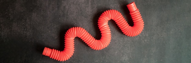 Foto bambini anti stress sensoriale pop tubo plastica fidget push giocattolo su un tavolo nero o sullo sfondo del pavimento. piccoli giocattoli poptube per bambini tonalità rossa colore brillante. bandiera. vista dall'alto, disposizione piatta